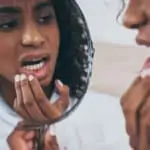 woman with tooth pain examines her teeth in mirror